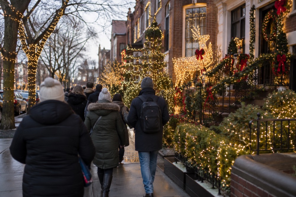 A guided group walking past houses covered in elaborate Christmas light displays in Brooklyn