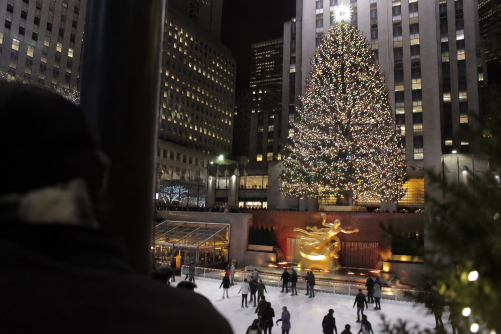 The Rockefeller Center Christmas tree glowing above skaters on an ice rink at night