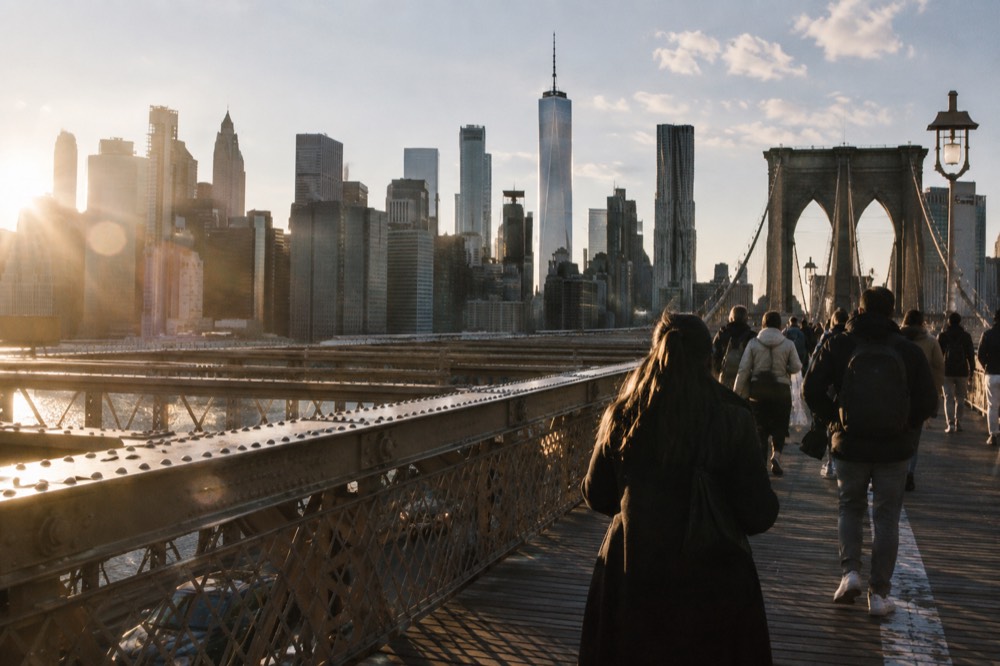 Visitors walking across the Brooklyn Bridge promenade with the Manhattan skyline behind them