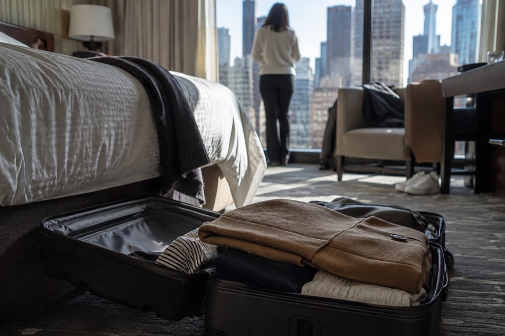 A packed suitcase open on a hotel room floor with coats folded on top