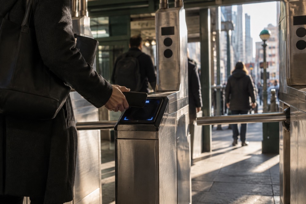 A subway turnstile with a rider tapping a phone on the reader
