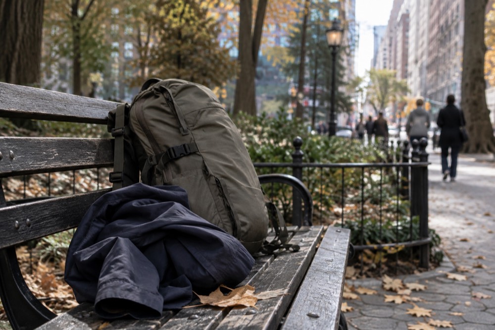 A packed daypack and folded rain jacket resting on a park bench beside autumn leaves