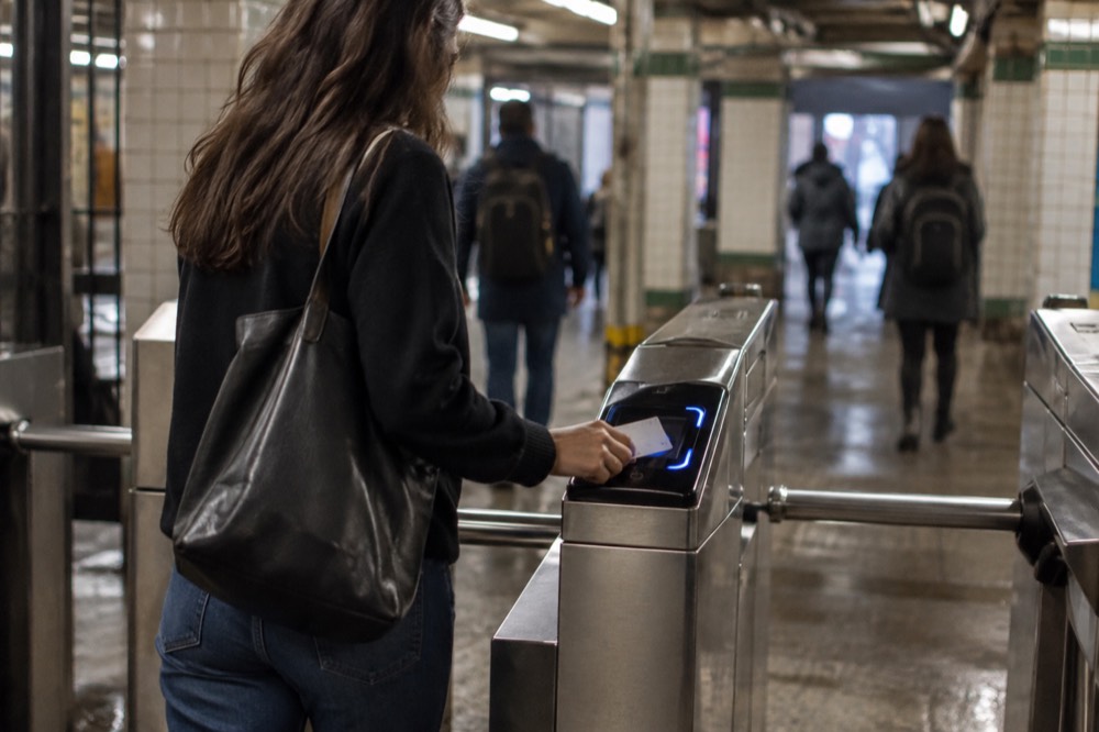 A rider tapping a contactless card at a subway turnstile in a tiled station