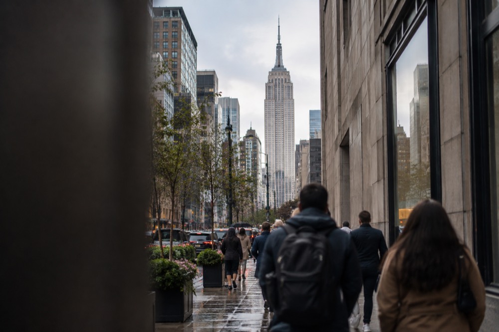 Visitors walking past the Empire State Building on a busy Midtown Manhattan sidewalk