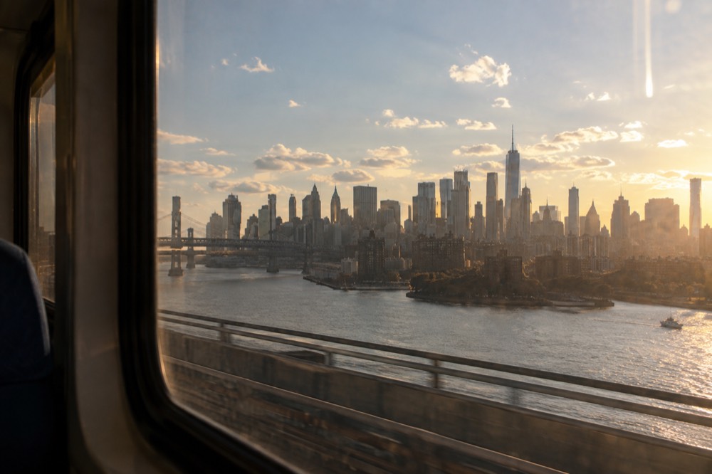 The Manhattan skyline seen from a train window crossing toward the city at golden hour