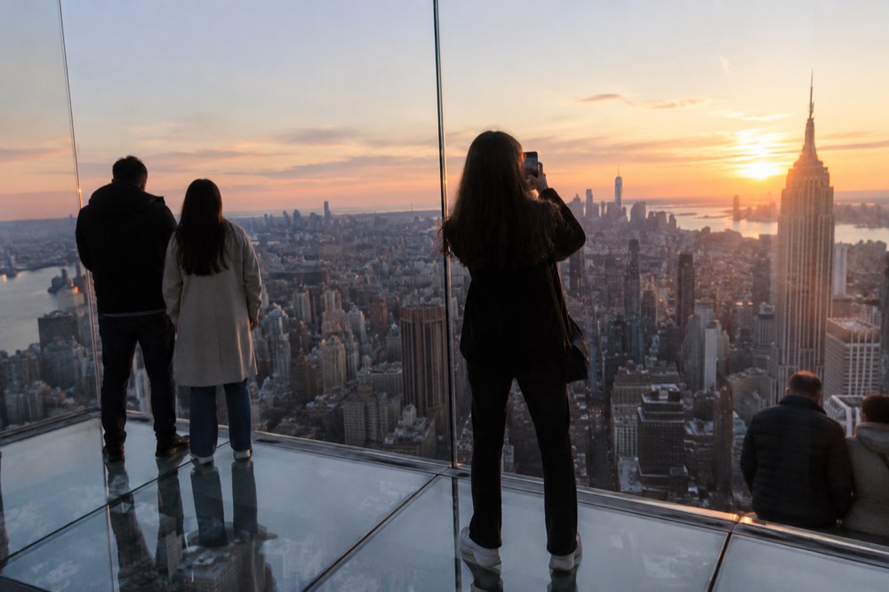 Visitors on a glass-floored observation deck above the city at dusk