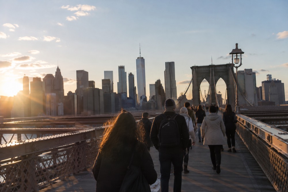 Pedestrians crossing the Brooklyn Bridge walkway with the skyline behind