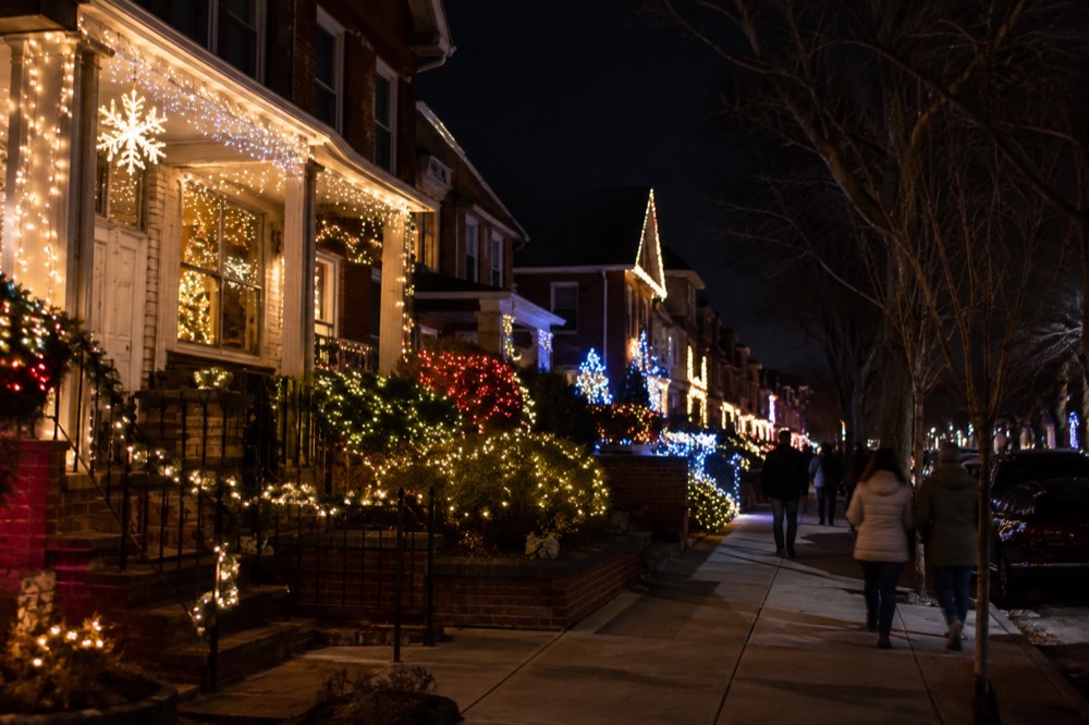 A residential Brooklyn block at night with houses covered in colorful holiday lights and visitors walking