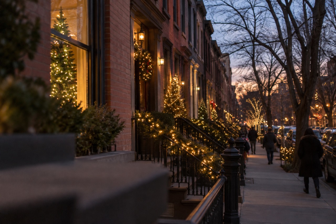 A Brooklyn street lined with houses covered in glowing Christmas light decorations at dusk
