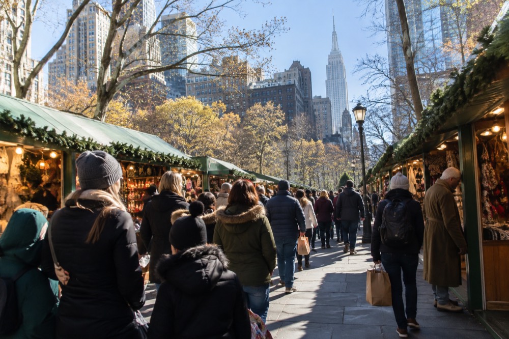 Families and shoppers walking between holiday market stalls in a Manhattan park