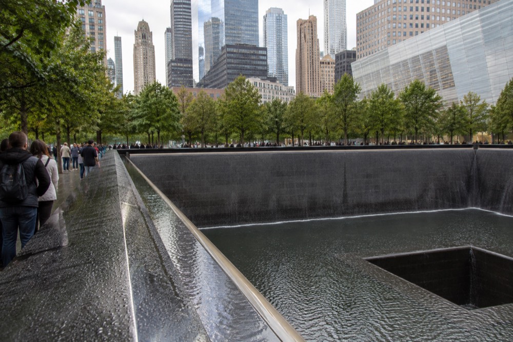 A quiet reflecting pool at the 9/11 Memorial surrounded by visitors standing in silence