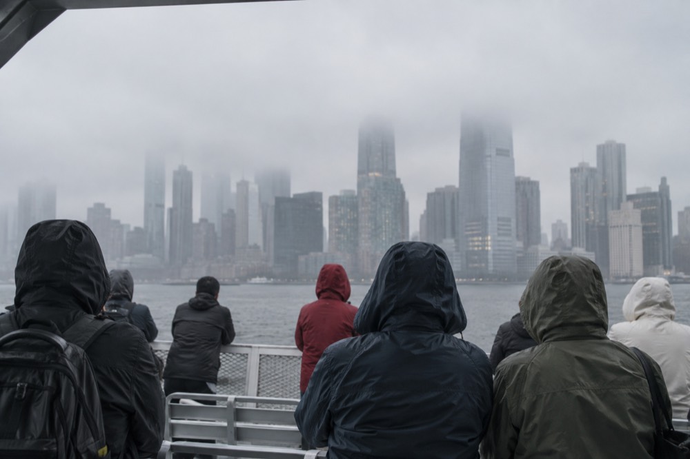 Ferry passengers in rain jackets on an open deck with fog over the harbor