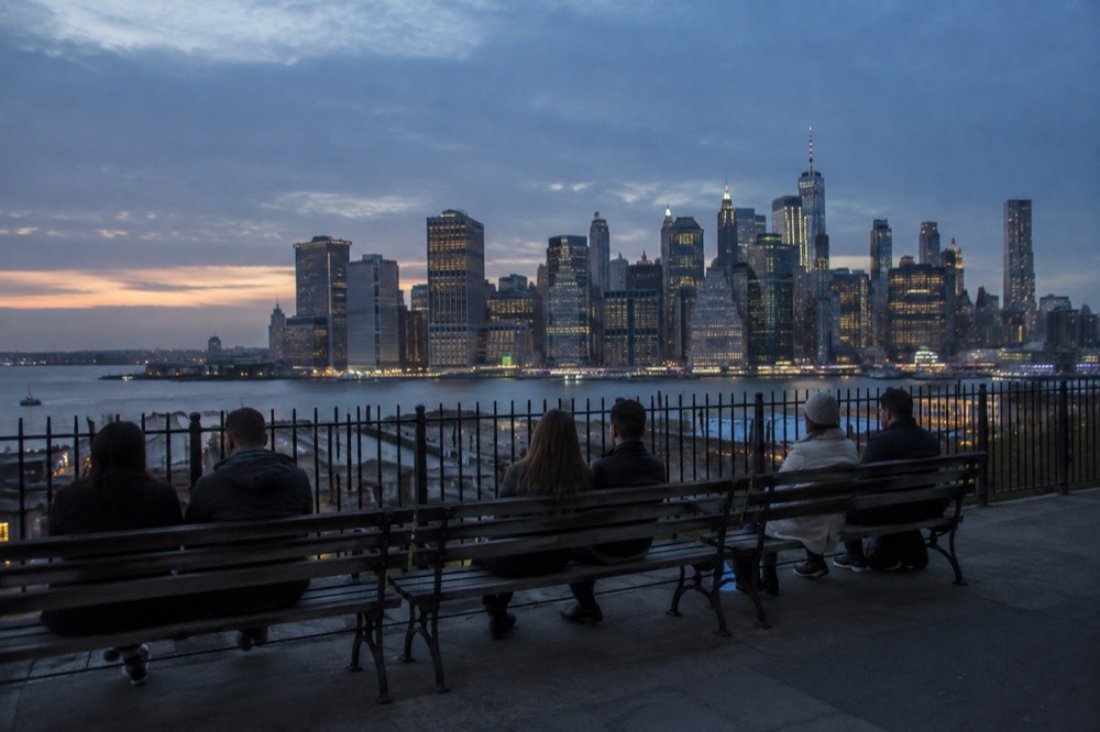 The Brooklyn Heights Promenade with people sitting on benches facing the Manhattan skyline