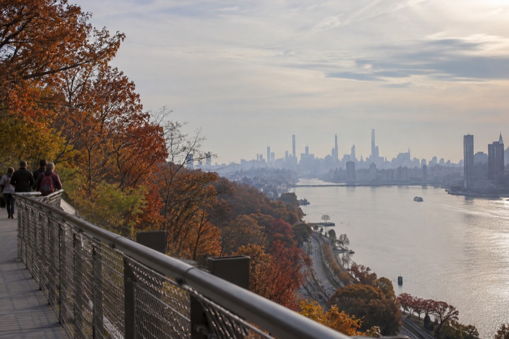 A river valley with hills covered in red and orange trees seen from an elevated walkway