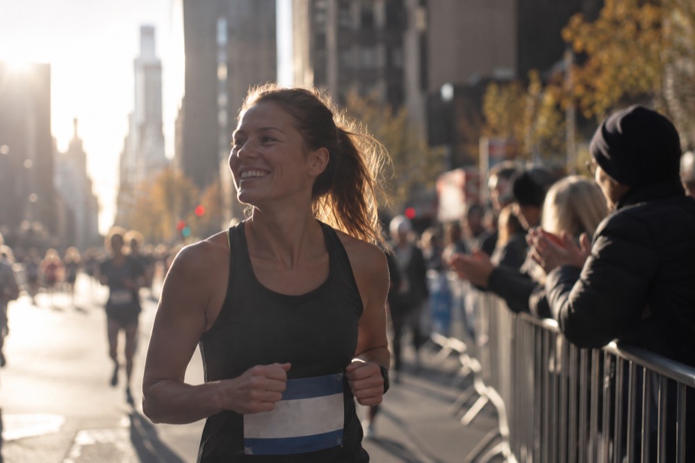 A runner wearing a race bib smiling while spectators clap behind a barrier