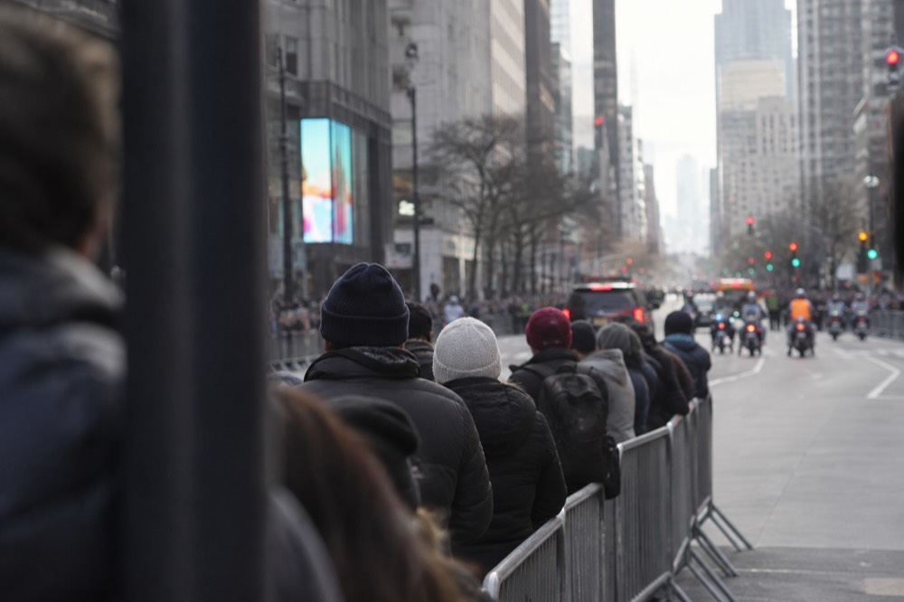 Spectators in jackets and hats watching from behind a metal barrier