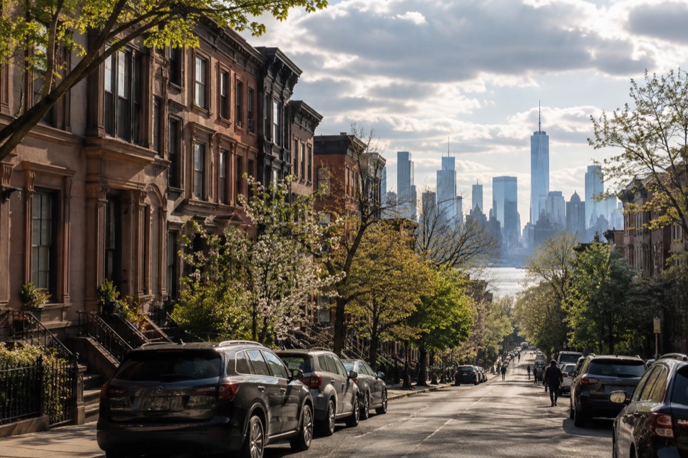 Brownstone row houses on a tree-lined Brooklyn street with the Manhattan skyline behind them