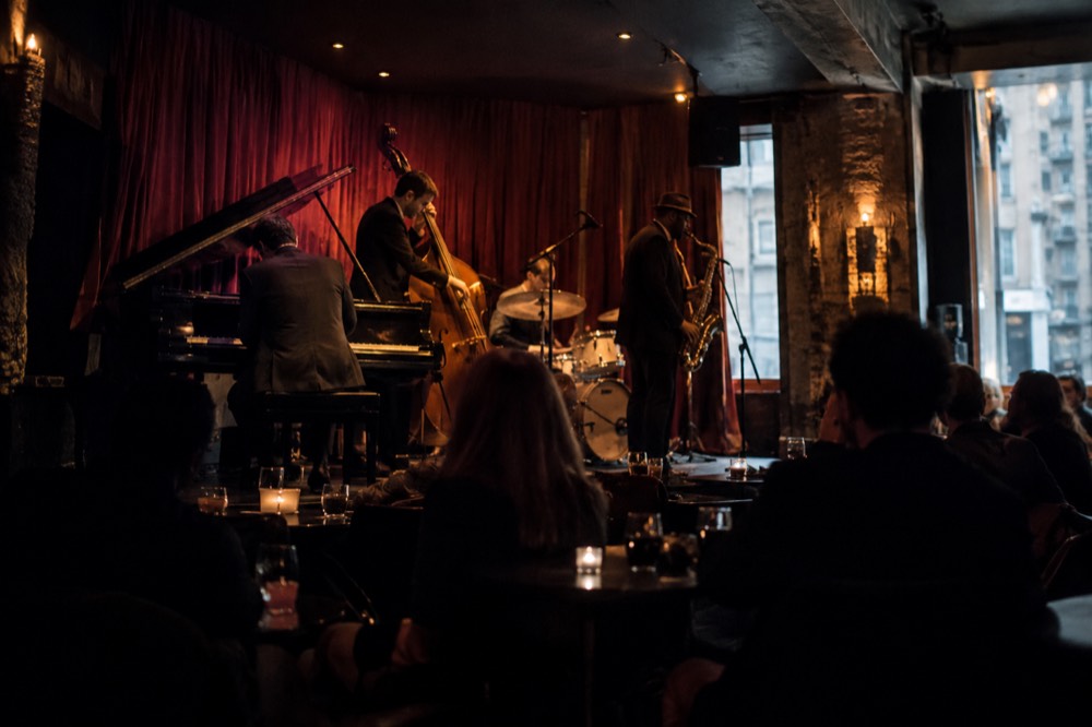 A dim jazz club interior with a small band playing on a low stage