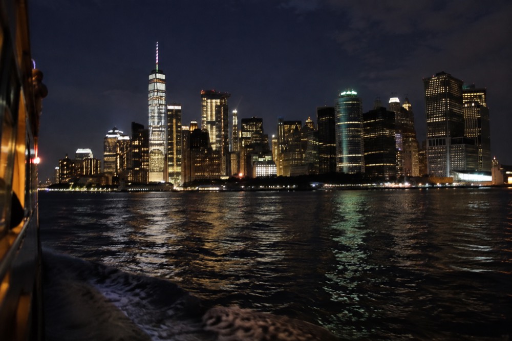 The Manhattan skyline lit up at night seen from the water, with reflections on the river