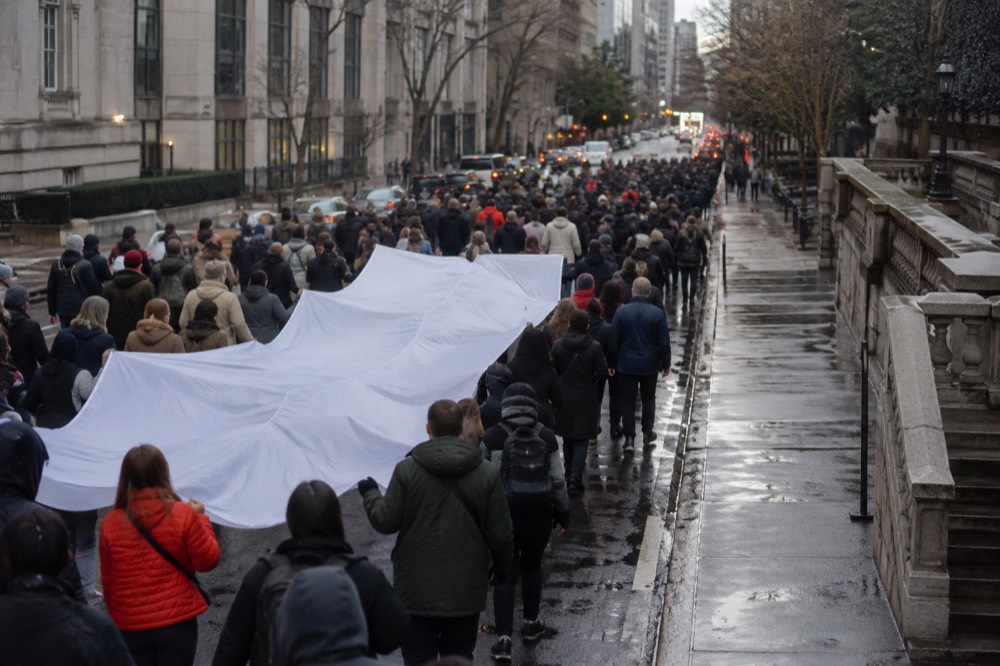 Marchers carry a large banner down a Manhattan avenue flanked by barricades and spectators