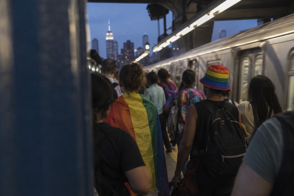 A crowded subway platform with rainbow-clad riders waiting for a train