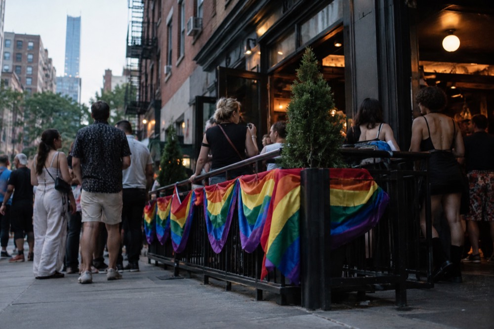 People celebrate at a bar entrance decorated with rainbow bunting in the evening