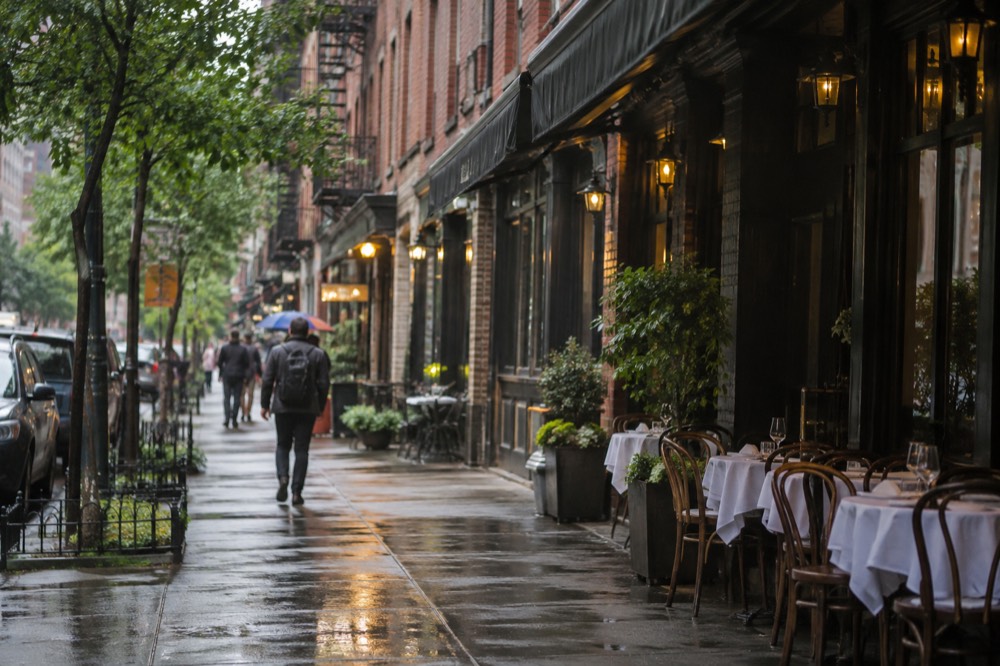 A row of brick restaurant fronts with awnings on a New York street at dusk