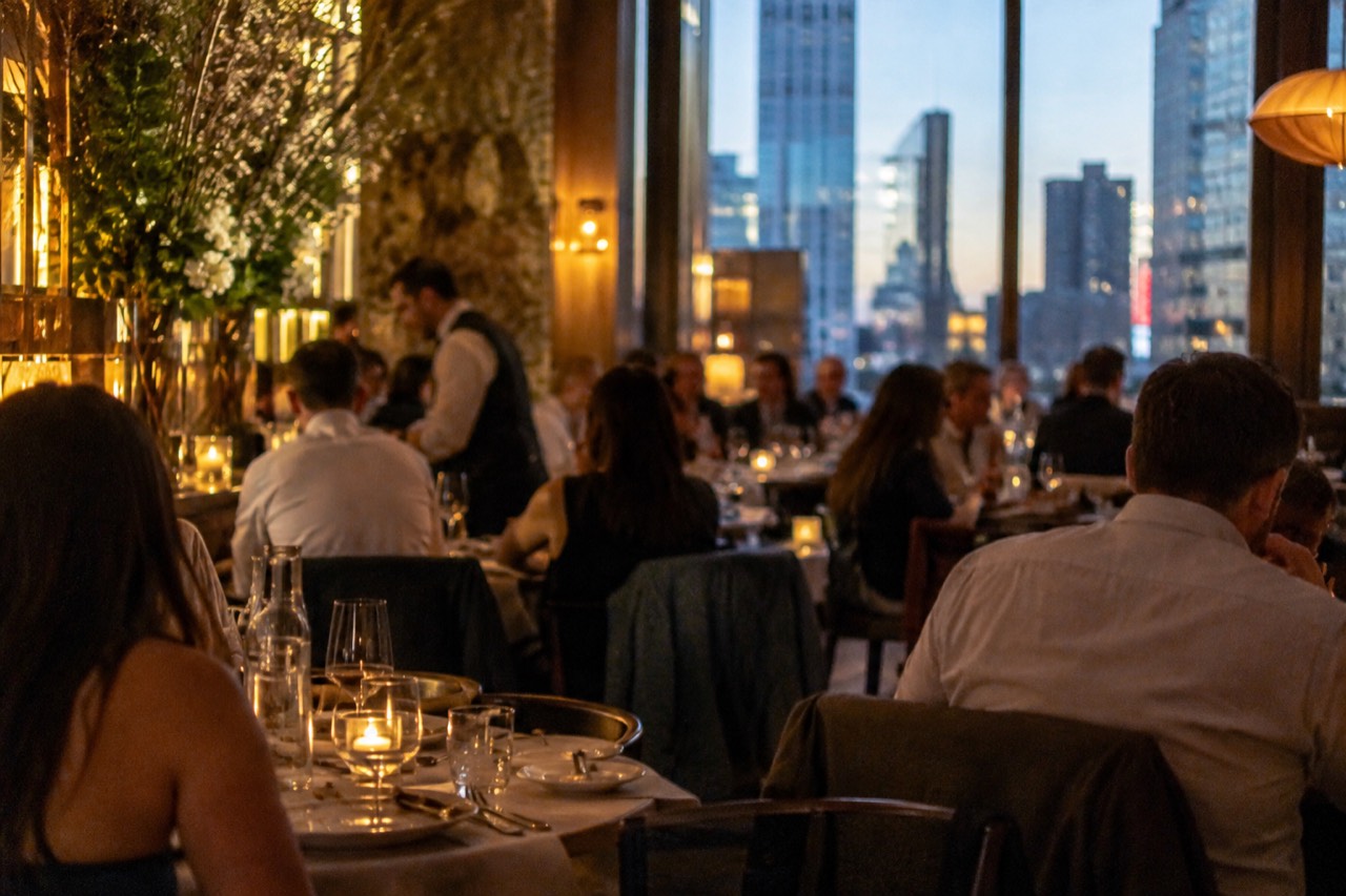 A busy New York restaurant dining room at dinner with tables set and warm lighting