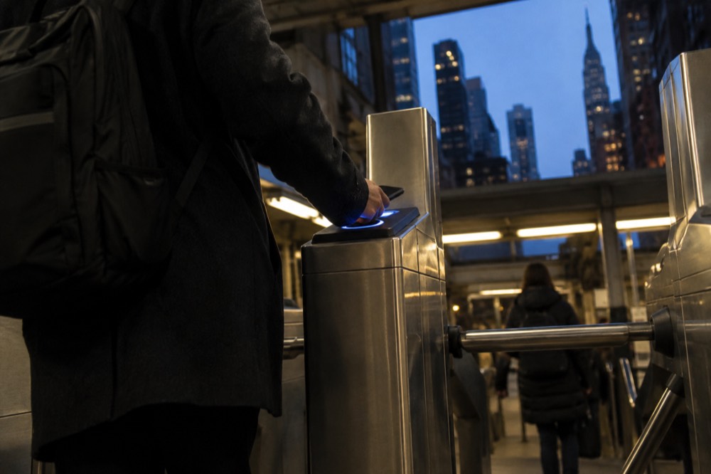 A commuter tapping a phone on an OMNY reader at a subway turnstile