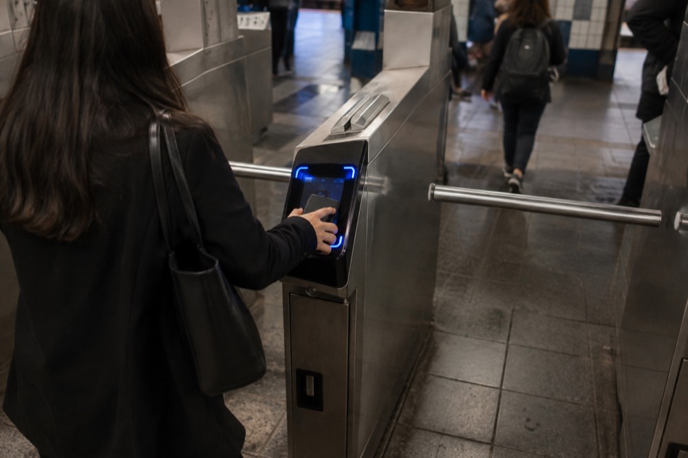 A turnstile in a New York subway station with a rider tapping a phone on the OMNY reader