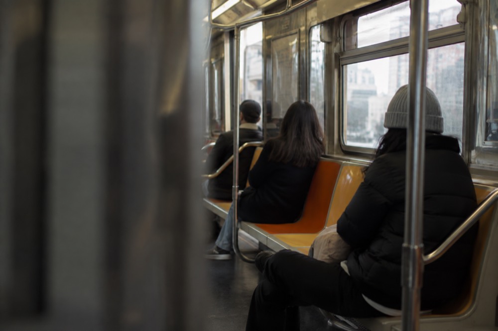A subway car interior with riders seated under orange and yellow seats