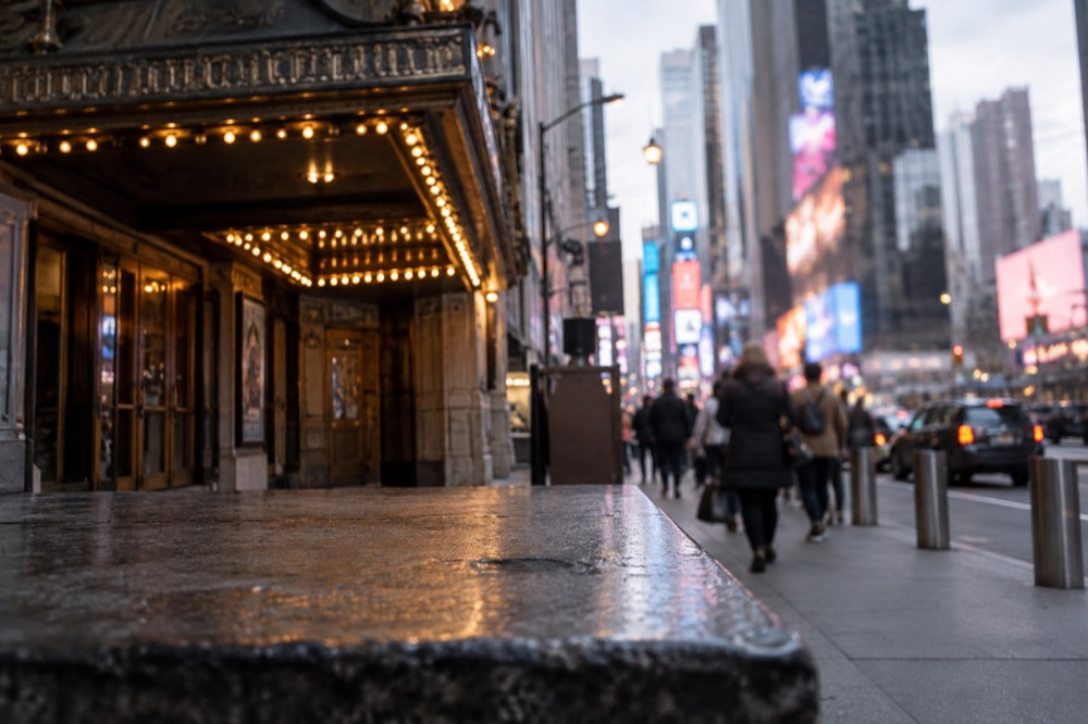 A small New York theater marquee glowing over a quiet street at dusk