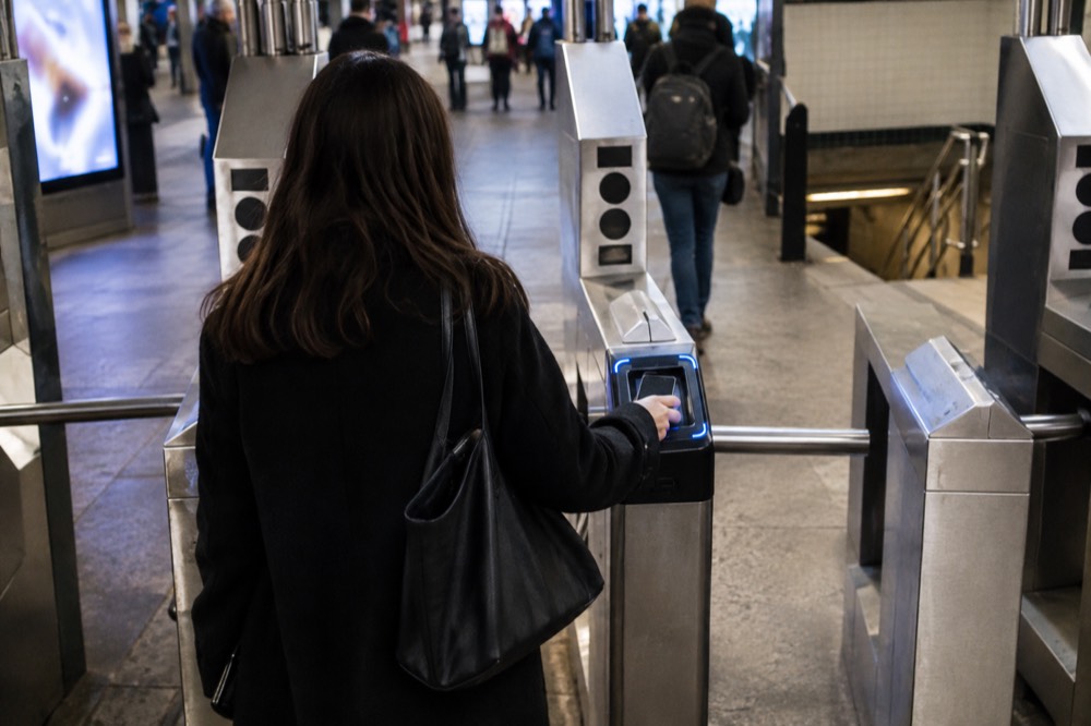 A subway turnstile in a New York station with a rider tapping a phone on the OMNY reader