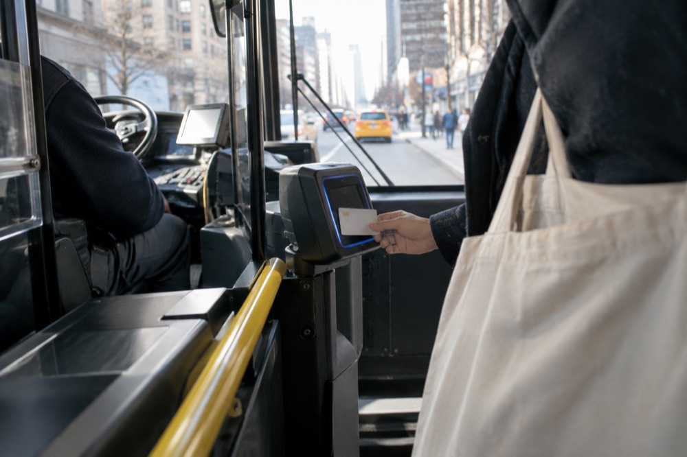 A passenger tapping a contactless bank card on a bus fare reader beside the driver