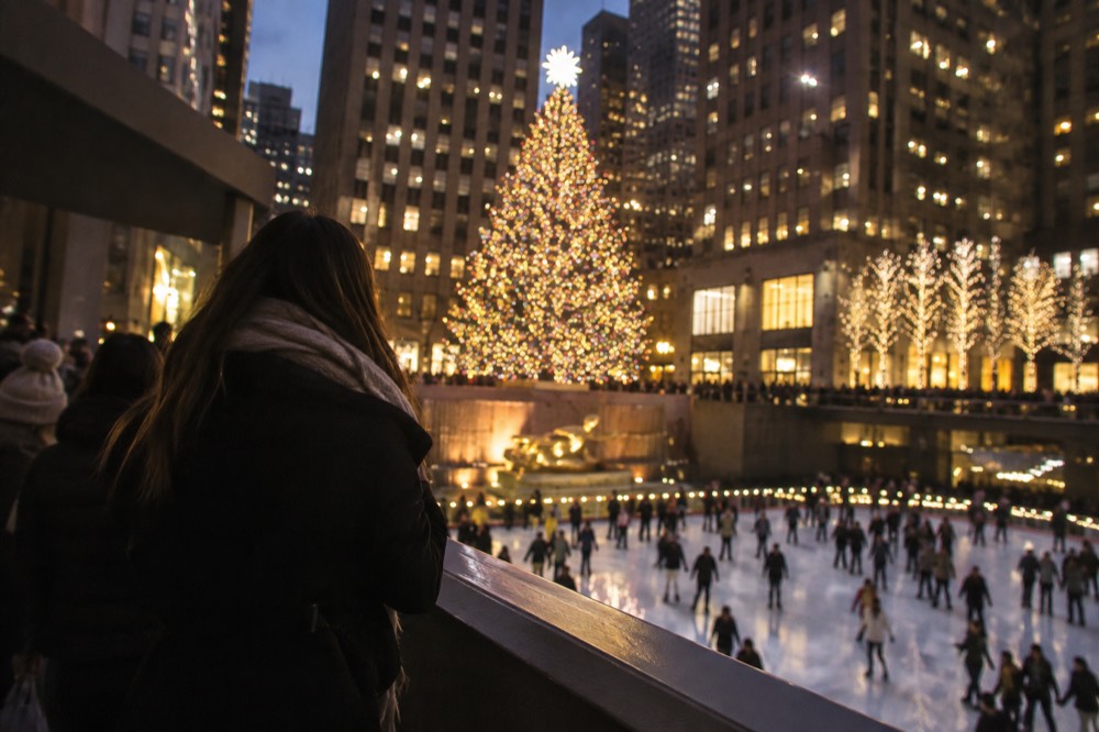 A large illuminated Christmas tree glowing above an ice rink surrounded by skyscrapers at night