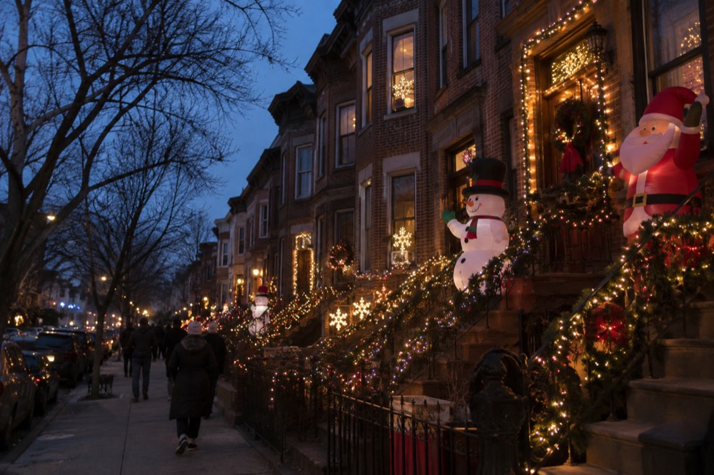 Rows of Brooklyn houses decorated with strings of Christmas lights and inflatable figures at night