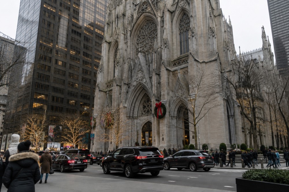 A gothic cathedral facade with holiday decorations seen from a busy avenue in winter