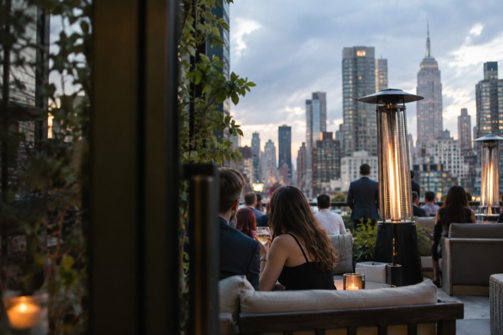 Guests in smart-casual evening clothes seated at a rooftop bar with heaters and lounge furniture
