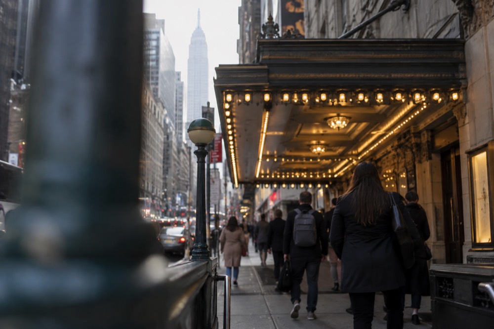 A Broadway theater marquee glowing above a crowded sidewalk in Midtown Manhattan at night