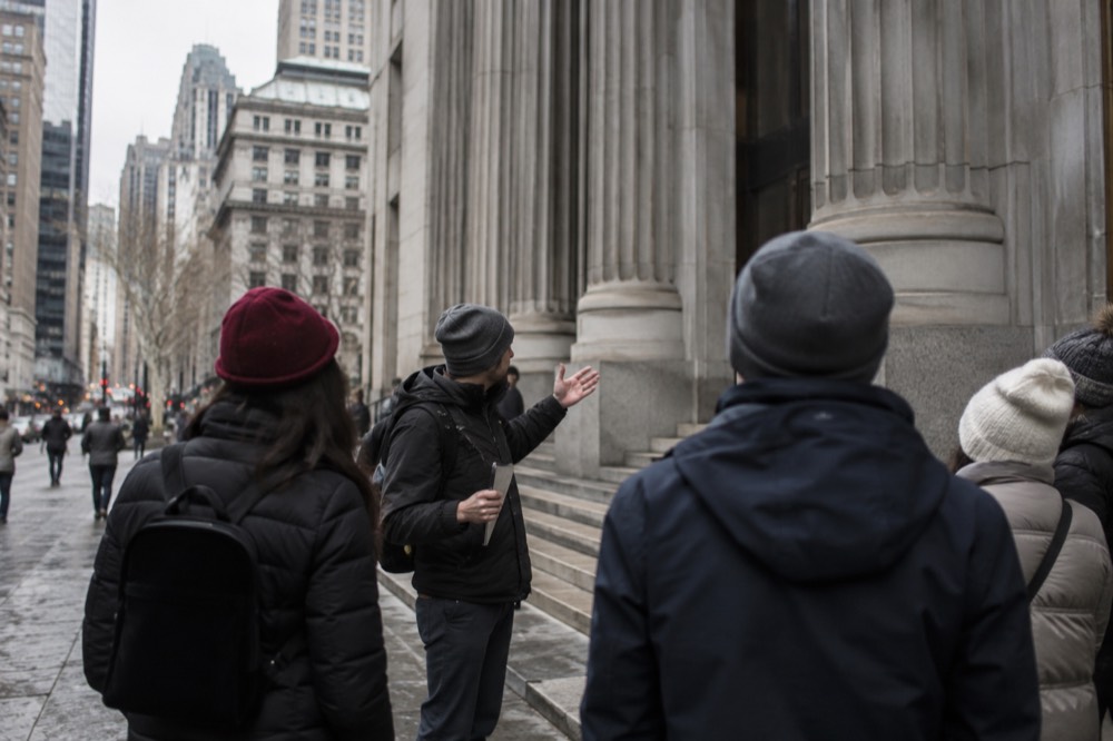 A guide speaking to a small group of visitors beside a historic Lower Manhattan building