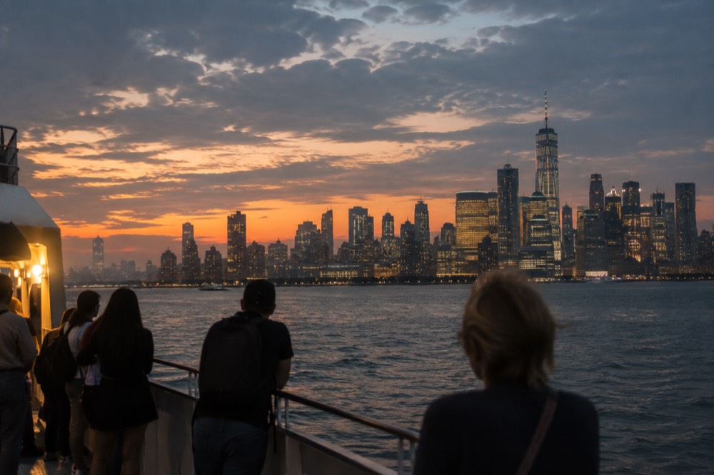A boat deck at dusk with the Manhattan skyline and lit skyscrapers behind it