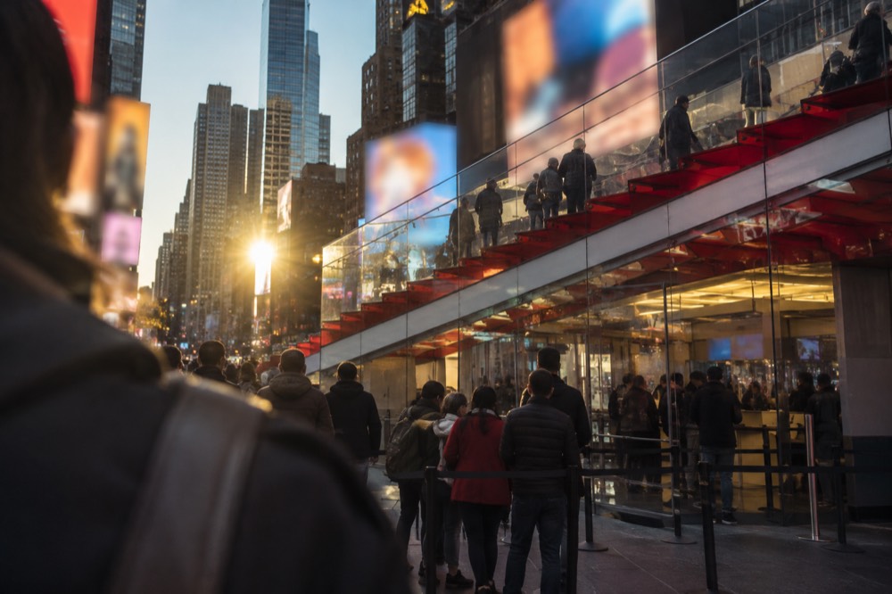 The TKTS booth in Times Square under its red steps at dusk with a short queue of people