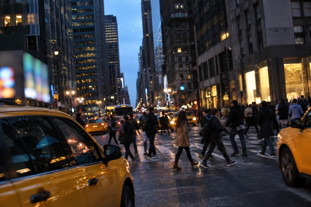 Pedestrians crossing a busy Midtown street with yellow taxis in the foreground