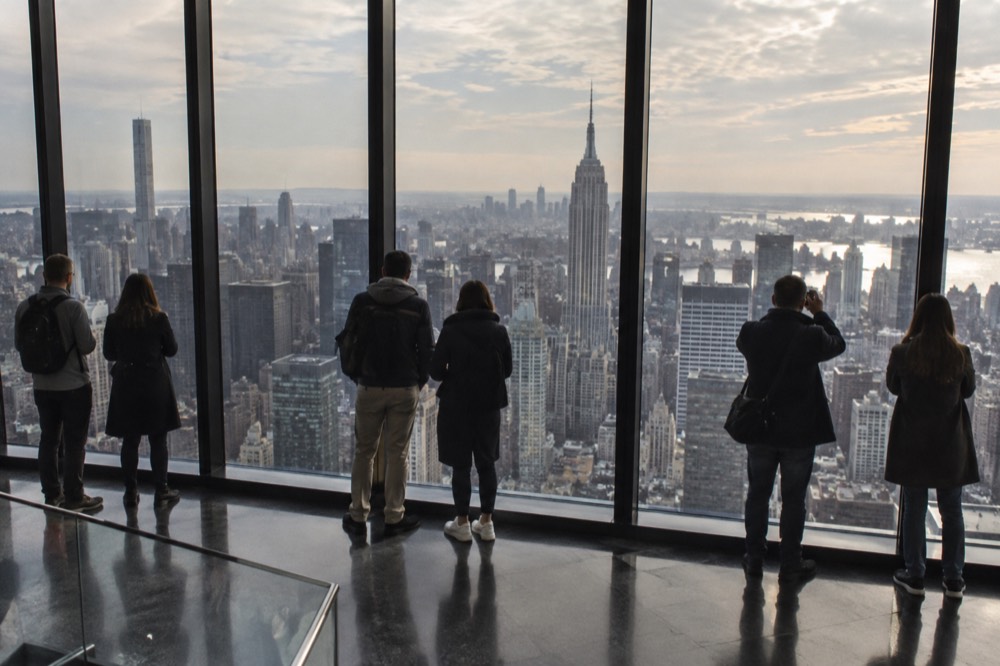 Visitors looking out through floor-to-ceiling windows at a city skyline from a high observation deck