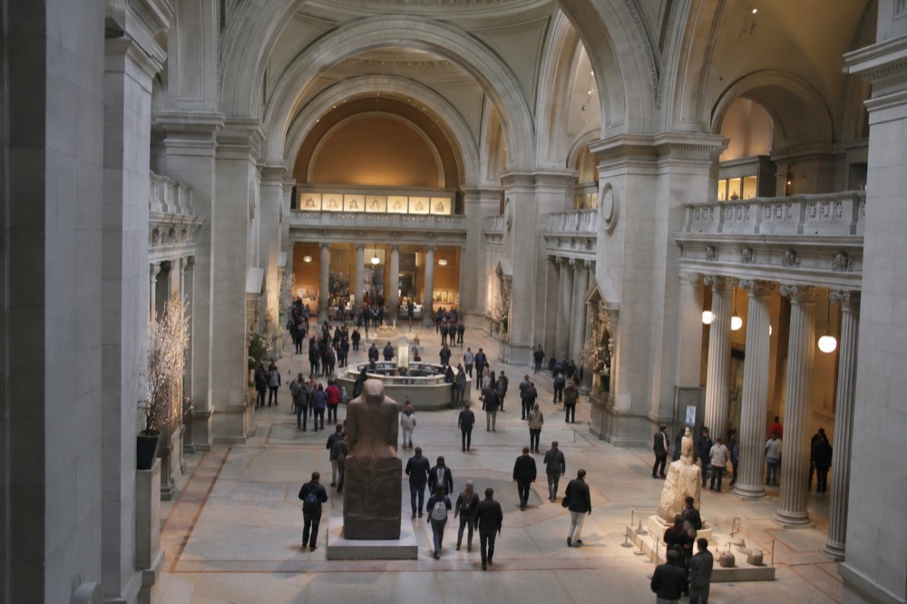 A grand museum gallery with visitors walking beneath tall arched ceilings