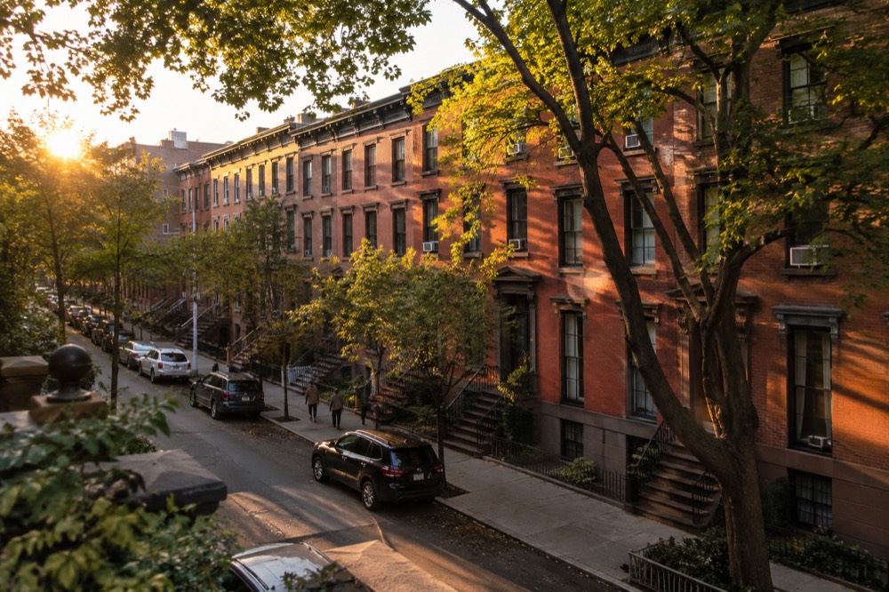 A row of brick townhouses on a quiet Brooklyn street with trees along the sidewalk