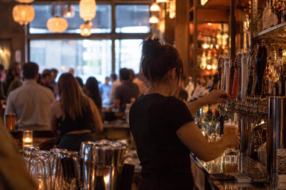 A bartender pouring a beer at a crowded New York bar with warm lighting