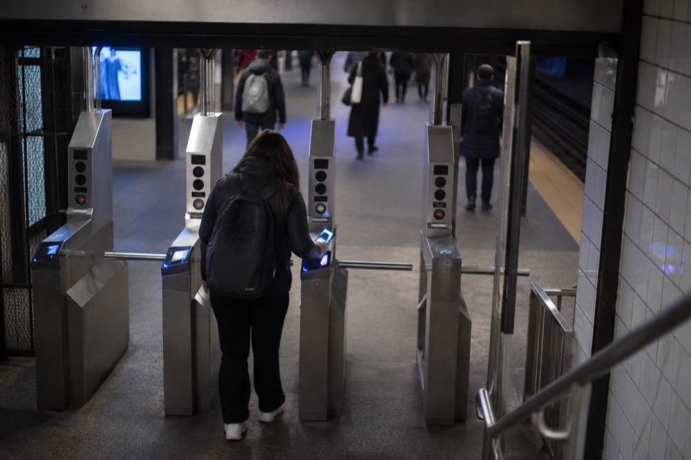 A commuter tapping a phone at a subway turnstile in a New York station