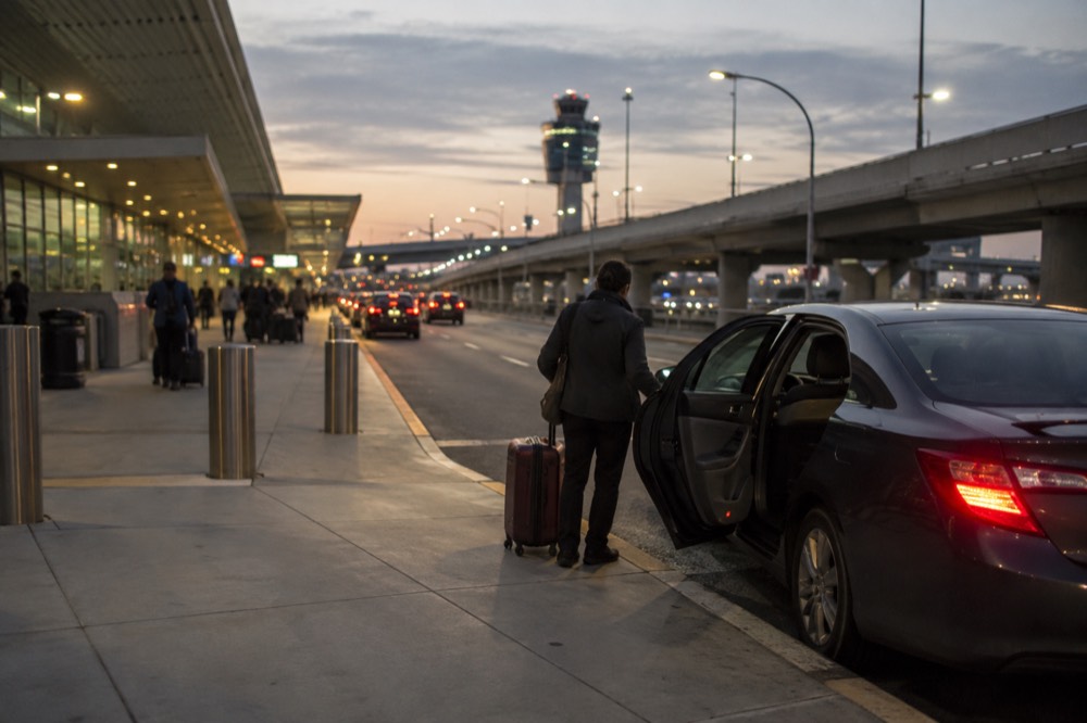 A private car waiting at a designated pickup curb outside an airport terminal at dusk