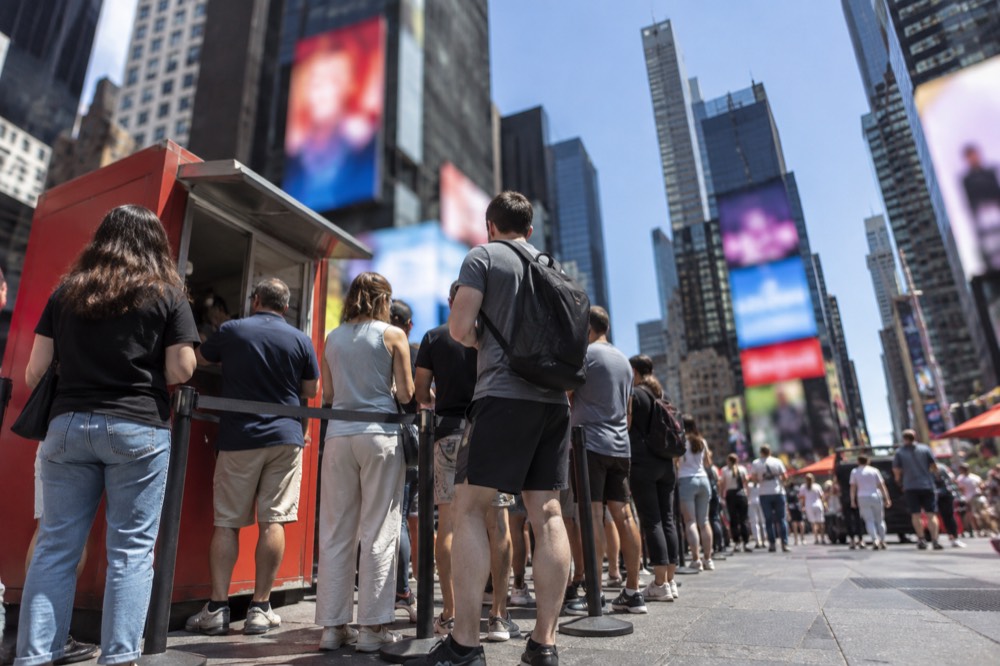 A line of people waiting at an outdoor discount ticket booth in a city square